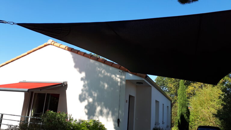 Voile d’ombrage tendue noire fixée sur la façade d’une maison blanche pour une protection solaire élégante